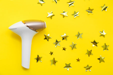 Composition with modern photoepilator and golden stars on yellow backgroundの写真素材