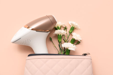 Cosmetic bag with modern photoepilator and carnation flowers on color background, closeupの写真素材