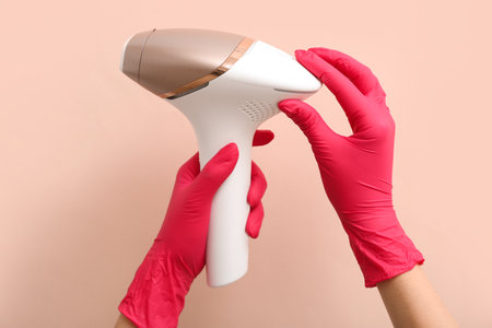 Woman in rubber gloves holding modern photoepilator on color background, closeupの写真素材