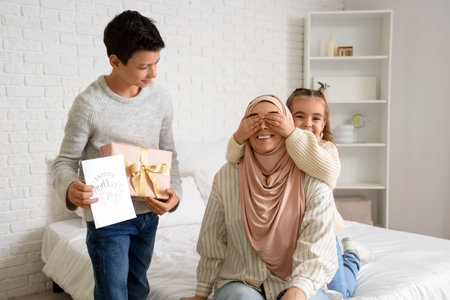 Little children greeting their Muslim mother with gifts in bedroomの写真素材