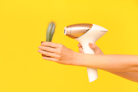 Hands of woman with photoepilator and cactus on yellow backgroundの写真素材