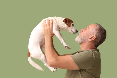Senior man playing with cute dog on green backgroundの写真素材