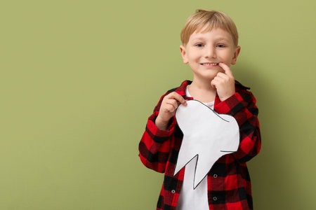 Happy little boy with healthy teeth and paper tooth on green background