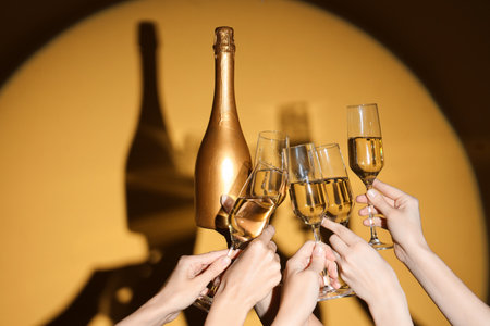 Female hands with bottle and glasses of champagne on yellow backgroundの写真素材