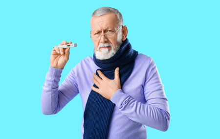 Old man with sore throat holding thermometer on blue background