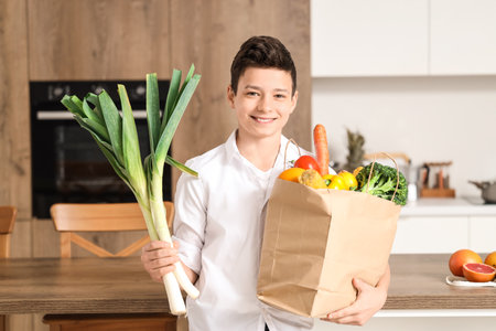 Cute little boy holding paper bag with different vegetables in kitchenの写真素材