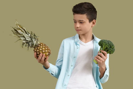Cute little boy with broccoli and pineapple on green backgroundの写真素材