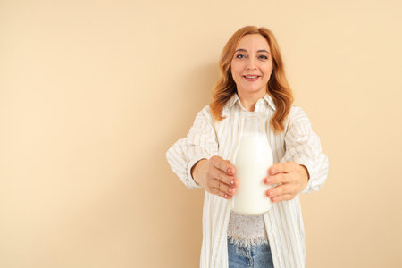 Mature woman with bottle of milk on beige backgroundの写真素材