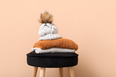 Stack of folded sweaters with hat on chair against beige backgroundの写真素材