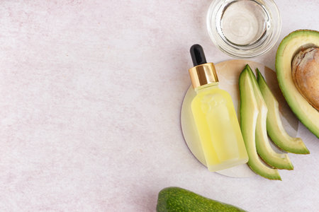 Fresh avocado with glass bowl and bottle of essential oil on beige background