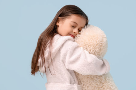 Cute little happy girl in bathrobe with pillow on blue backgroundの写真素材