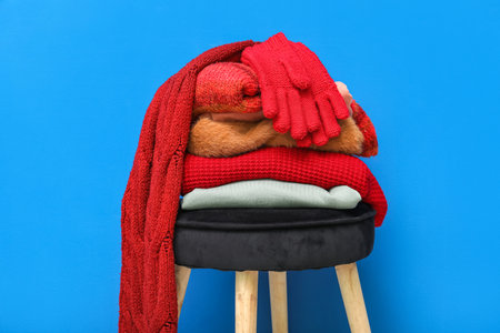 Stack of folded sweaters with scarf and gloves on chair against blue backgroundの写真素材