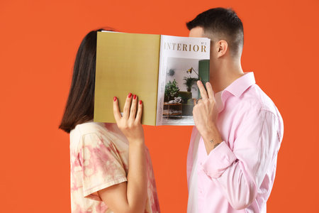 Young couple with magazine on orange backgroundの写真素材