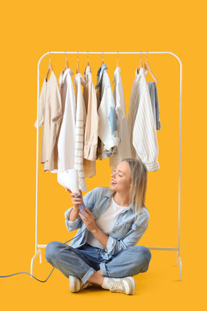 Pretty young woman with modern steamer and clothes on yellow backgroundの写真素材