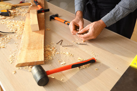 Mature carpenter with nails at table in workshop, cl