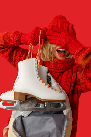 Funny young woman with ice skates and bag on red backgroundの写真素材
