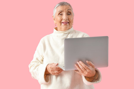 Senior woman with laptop on pink backgroundの写真素材