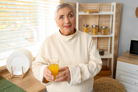 Senior woman with glass of juice in kitchenの写真素材