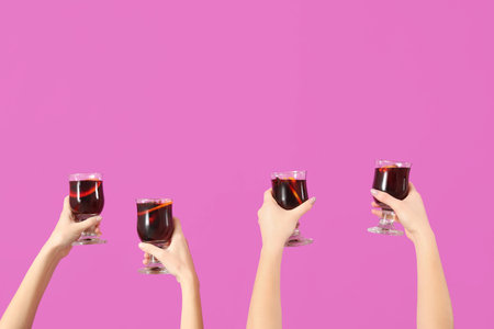 Female hands with glasses of warm mulled wine on pink backgroundの写真素材