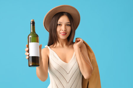 Young Asian woman with bottle of wine on blue backgroundの写真素材