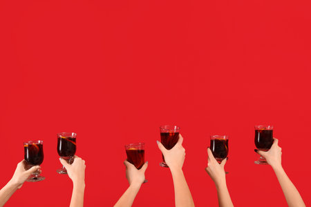 Female hands with glasses of warm mulled wine on red backgroundの写真素材