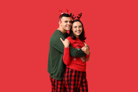 Happy young couple in Christmas pajamas hugging on red backgroundの写真素材