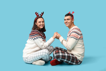 Happy young couple in Christmas pajamas sitting against blue backgroundの写真素材