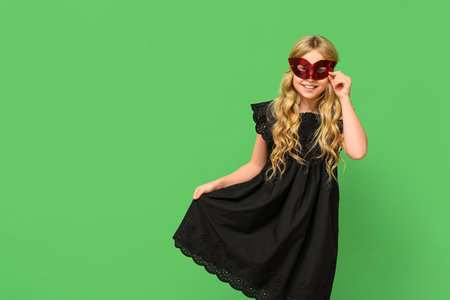 Happy little girl wearing carnival mask on green backgroundの写真素材