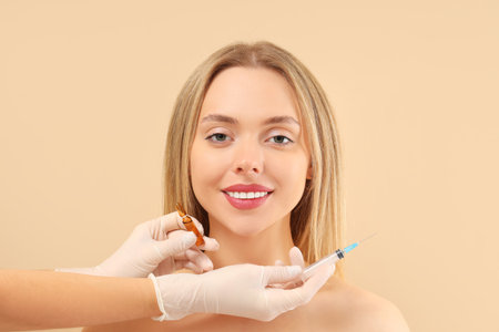Young woman receiving filler injection in face against beige background. Skin care conceptの写真素材