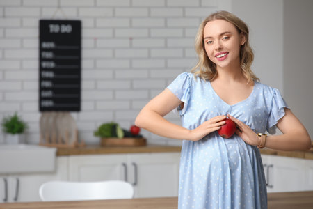 Young pregnant woman with apple in kitchenの写真素材