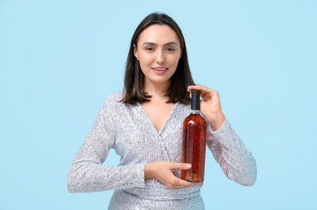 Beautiful young woman with bottle of red wine on blue backgroundの写真素材