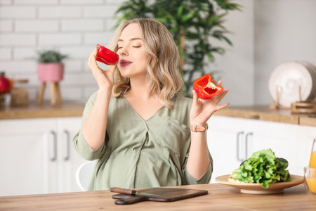Young pregnant woman with cut bell pepper at table in kitchenの写真素材