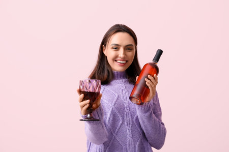 Beautiful young woman with glass and bottle of red wine on pink backgroundの写真素材