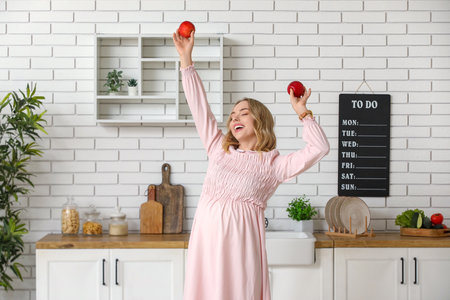 Happy young pregnant woman with apples in kitchenの写真素材