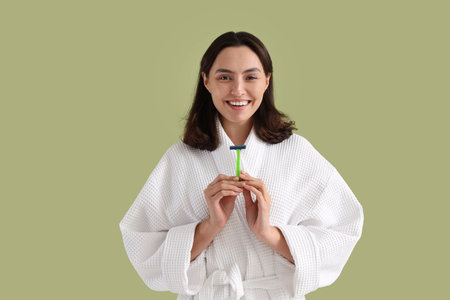 Beautiful young happy woman in bathrobe with razor on green backgroundの写真素材