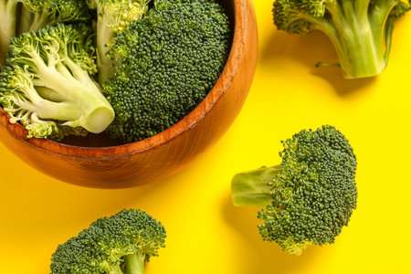 Wooden bowl with fresh broccoli cabbages on yellow background