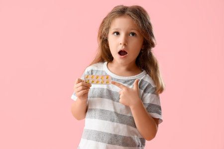 Shocked little girl pointing at pills on pink backgroundの写真素材