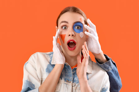 Young woman with painted face and male hand on orange background, closeup