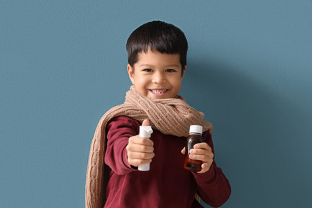 Ill little Asian boy with cough syrup and spray for sore throat on blue backgroundの写真素材