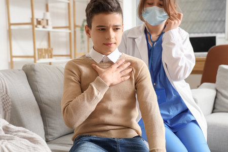 Doctor listening lungs of sick little boy with stethoscope at homeの写真素材