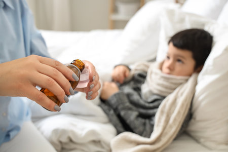Mother pouring cough syrup for her ill little son in bedroom, closeupの写真素材