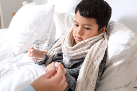 Ill little Asian boy taking pill from his mother in bedroomの写真素材