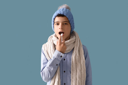 Sick little boy in hat using spray for sore throat on blue backgroundの写真素材