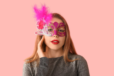 Beautiful young woman in carnival mask on pink backgroundの写真素材