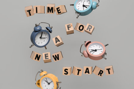 Flying cubes with text TIME FOR A NEW START and alarm clocks on gray background