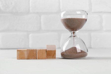 Wooden cubes with hourglass on table near white brick wall