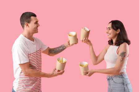 Young couple with French fries on pink backgroundの写真素材
