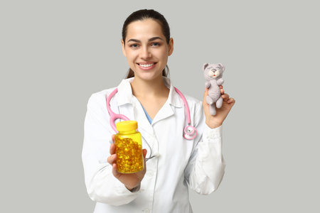 Portrait of female doctor with pills and plush toy on gray backgroundの写真素材