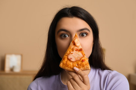 Young woman with a piece of tasty pizza at homeの写真素材