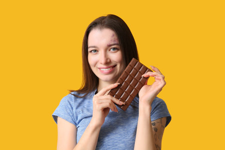 Young woman with chocolate bar on yellow backgroundの写真素材